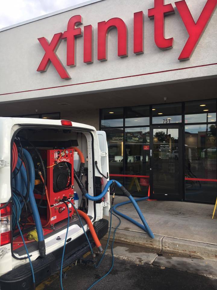 Carpet Cleaning Services in Salt Lake City - Father and Son Carpet Cleaning A van offering Carpet Cleaning services is parked outside an Xfinity store in Salt Lake City, with equipment and hoses running from the van into the building.