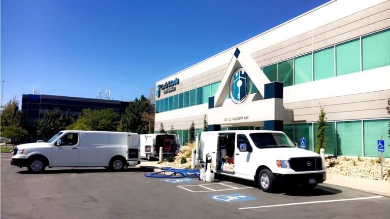 Professional Cleaning & Home Services in Holladay, Utah - Father and Son Carpet Cleaning Two white service vans are parked outside a modern office building with tinted windows in Holladay, Utah, where several handicap parking spaces are visible—showcasing reliable home and cleaning services for local businesses.