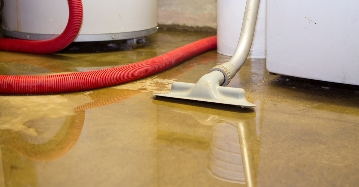 A vacuum hose is being used for water extraction in a flooded room, with a red hose and white machines in the background.