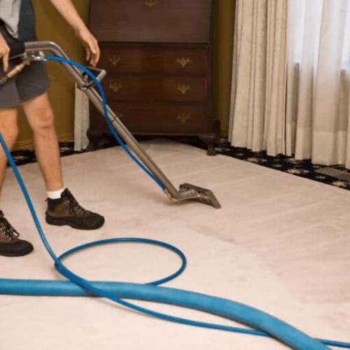 Why Carpet Stretching Matters More Than You Think - Father and Son Carpet Cleaning A person is cleaning a carpet with a professional carpet cleaning machine attached to a blue hose in a home setting, ensuring thorough flooring care and proper carpet maintenance.