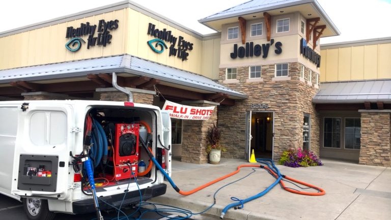 Carpet Cleaning & Home Services in Midvale, UT - Father and Son Carpet Cleaning A white van offering Home Services and Carpet Cleaning is parked outside Jolley’s pharmacy in Midvale UT. Hoses run inside the building, and a banner advertises flu shots.