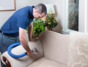 A man using a blue vacuum to clean a couch and remove stains.